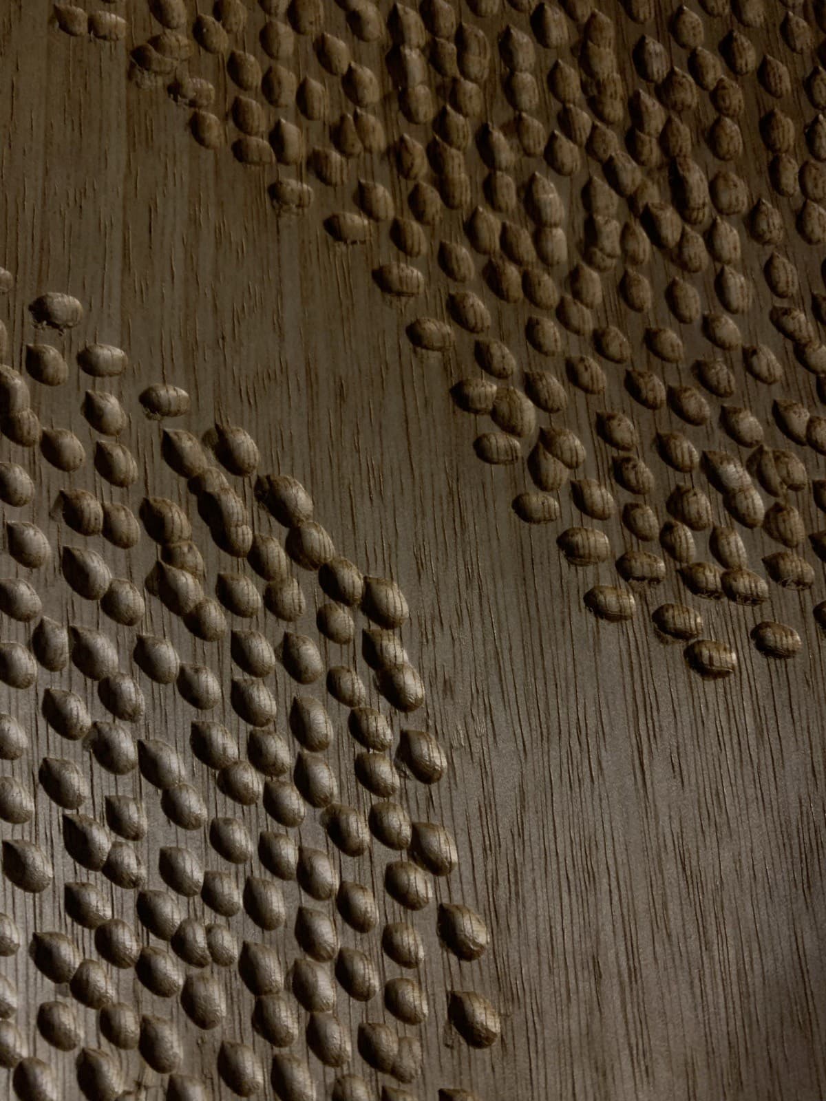Detail of a hand-carved, dimpled wood panel catching raking light